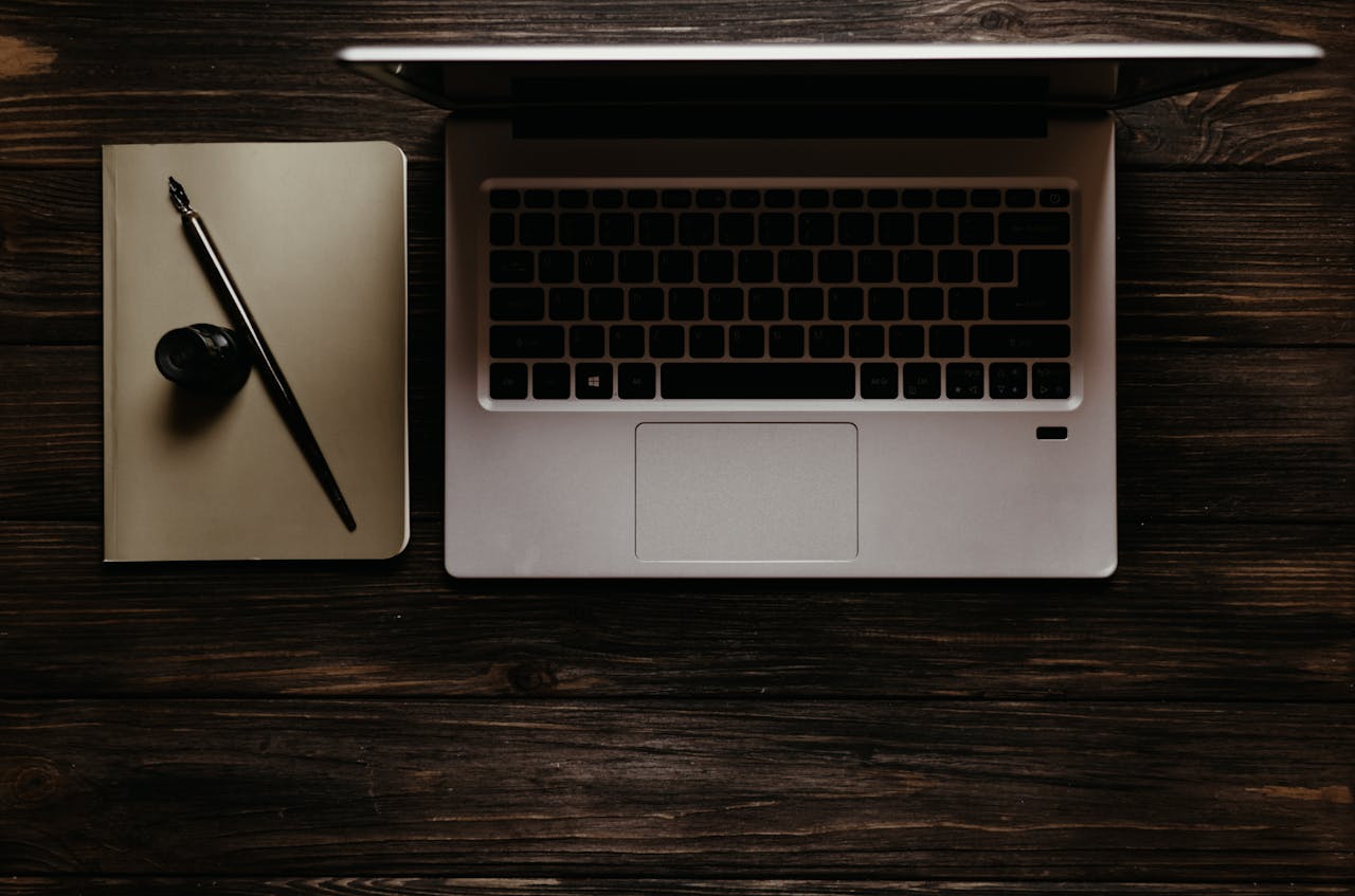 our-services-1 A stylish flat lay of a laptop with a notebook and fountain pen on a wooden desk.